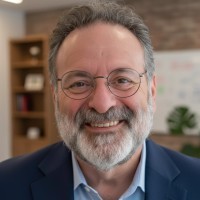 Professional headshot of Shel Holtz wearing glasses and smiling and wearing a dark blue suit jacket and light blue collared shirt.